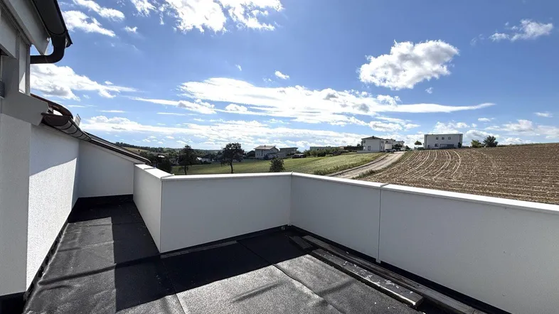 Unfertige Dachterrasse mit weitem Blick über die umliegende Landschaft und Felder unter blauem Himmel.