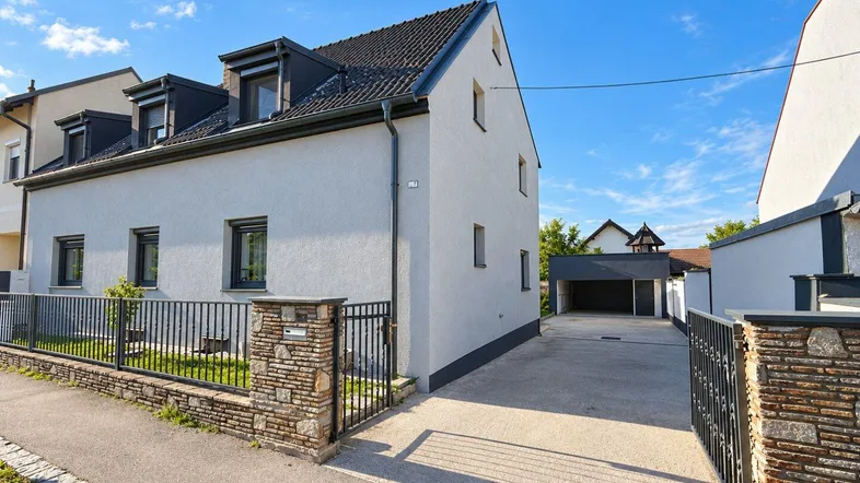 Modernes Einfamilienhaus mit heller Fassade, Satteldach und gepflegtem Vorgarten unter blauem Himmel.