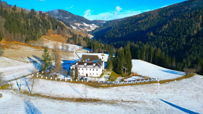 Historisches Gebäude in einer verschneiten Berglandschaft mit umliegenden Wäldern und klarem Himmel.