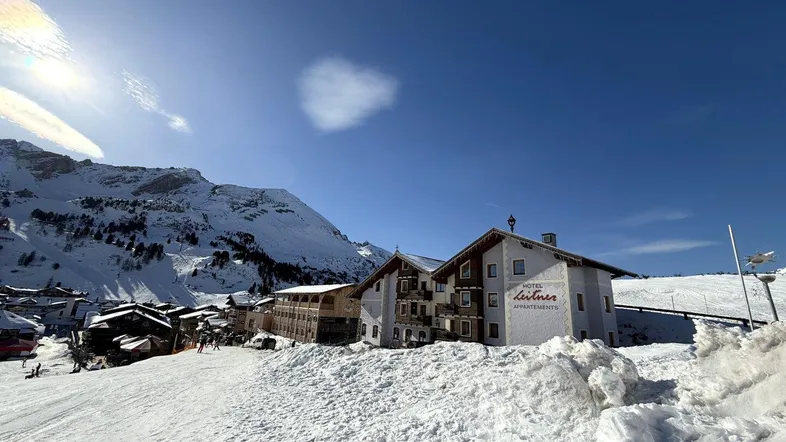 Hotelgebäude im Winter, umgeben von Schnee und Bergen unter blauem Himmel.