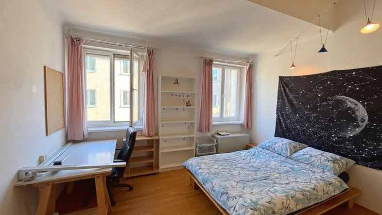 Helles Schlafzimmer mit Holzbett, Schreibtisch und Blick auf die umliegenden Gebäude.