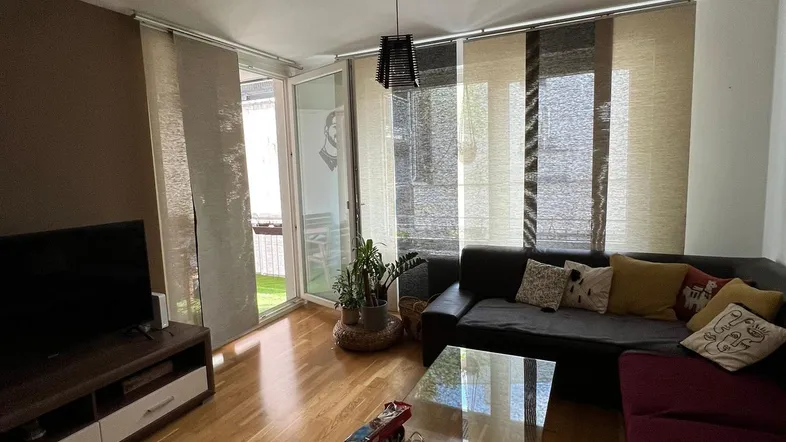 Helles Wohnzimmer mit Holzboden, großem Sofa und Zugang zu einem sonnigen Außenbereich.