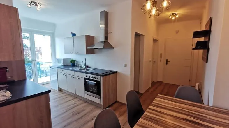 Moderne Küche mit Holzboden, integrierten Geräten und Essbereich, mit Zugang zum Balkon.