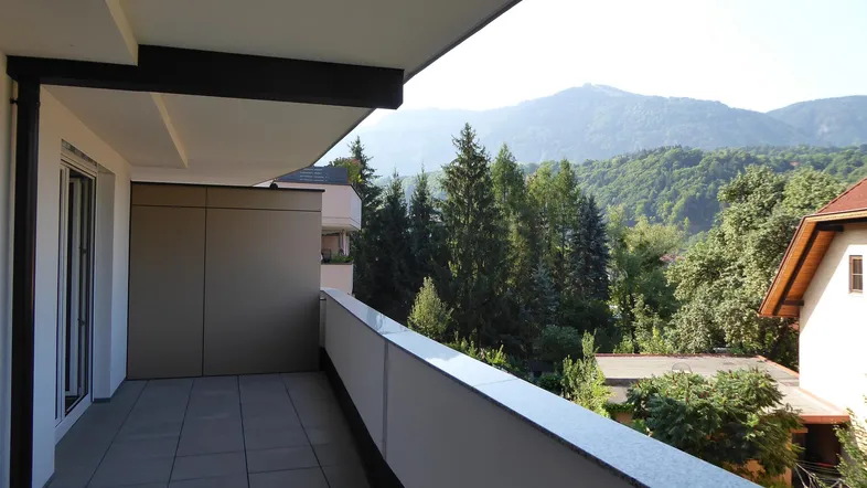 Geräumiger Balkon mit Fliesenboden und weitem Blick auf die umliegenden Berge und grüne Wälder.