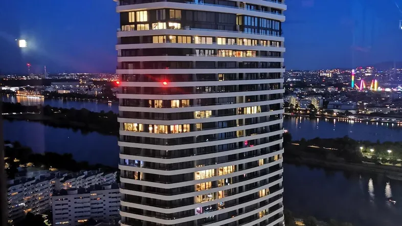 Moderner Wolkenkratzer bei Nacht mit beleuchteter Stadt und Fluss im Hintergrund.