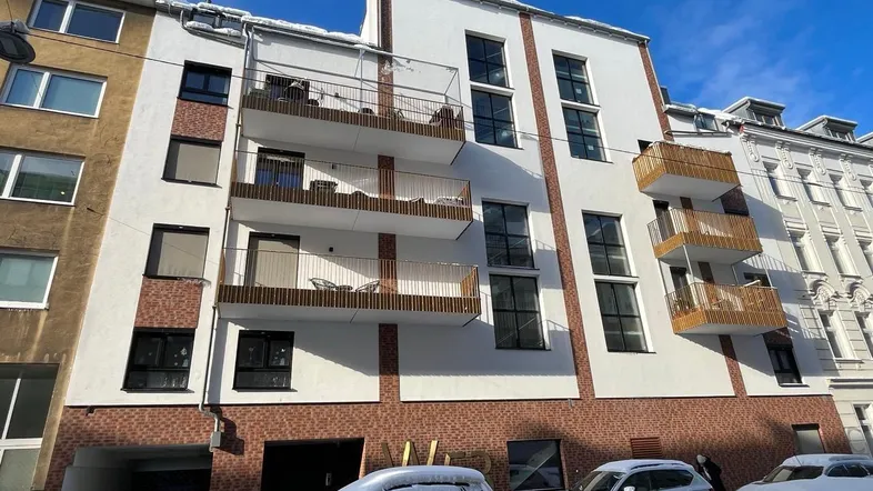 Moderne Wohnhausfassade mit Balkonen und Ziegelmauerwerk, bedeckt mit leichtem Schnee.