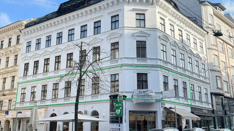 Historisches Eckgebäude mit weißer Fassade und Geschäften im Erdgeschoss an einer belebten Straße.