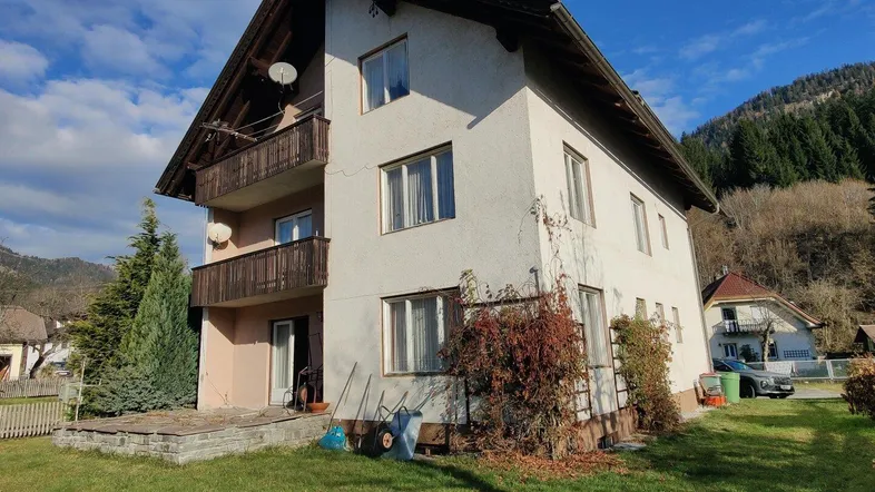 Mehrstöckiges Wohnhaus mit Balkonen und Gartenbereich in ländlicher Umgebung und Bergblick.
