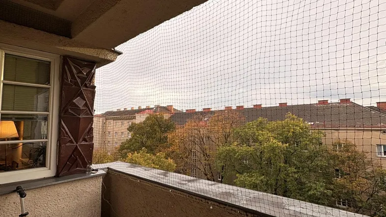 Balkon mit Sicherheitsnetz und Blick auf umliegende Gebäude und Bäume, ausgestattet mit einem Stuhl.