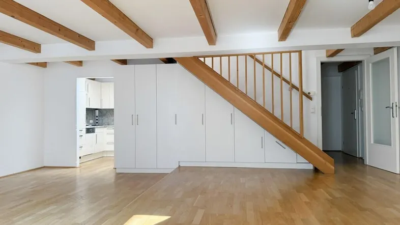 Helles Wohnzimmer mit Holzbalken, Parkettboden und integrierten Schränken unter der Treppe.