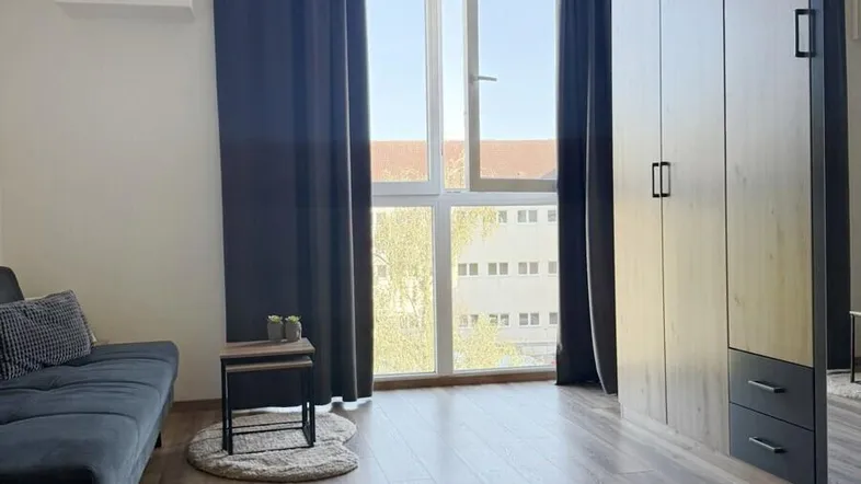 Helles Wohnzimmer mit Laminatboden, Sofa und großem Fenster mit Blick ins Grüne.