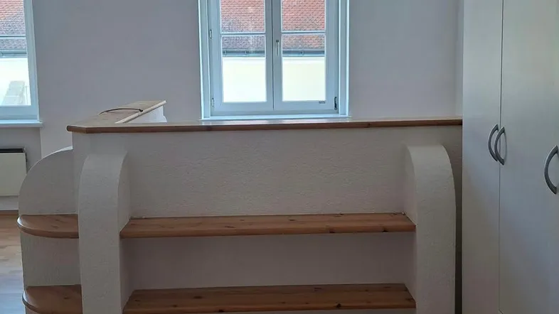 Helles Zimmer mit Holzboden, weißen Wänden und einem eingebauten Regal sowie einem Kleiderschrank.