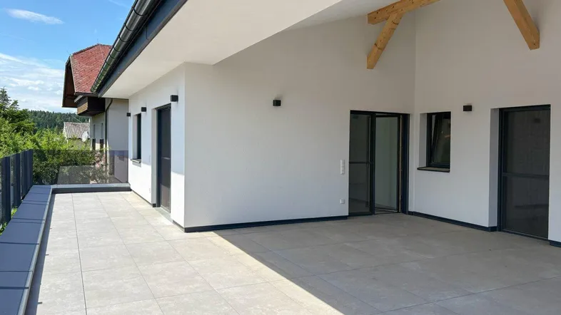 Große, geflieste Terrasse mit Holzbalken und Zugang zu mehreren Räumen, ideal für Entspannung im Freien.