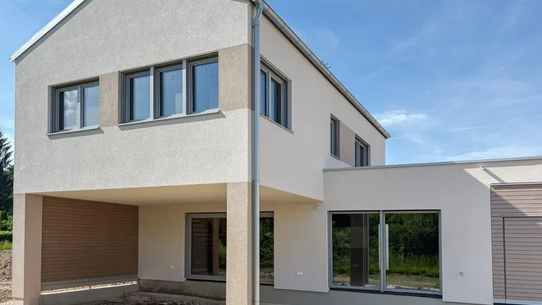 Modernes Einfamilienhaus im Bau mit Carport und großen Fenstern.
