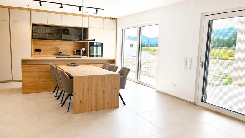 Heller offener Wohn- und Essbereich mit moderner Küche, Holzelementen und Zugang zur Terrasse.