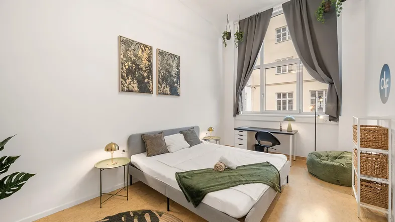 Helles Schlafzimmer mit großem Fenster, Schreibtisch und moderner Einrichtung.