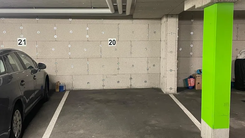 Tiefgaragenstellplatz mit Betonwänden, sichtbaren Rohren und leuchtend grünen Säulen.