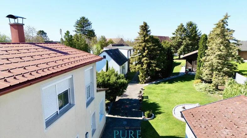 Luftaufnahme eines Hauses mit großem Garten und umliegenden Bäumen unter blauem Himmel.