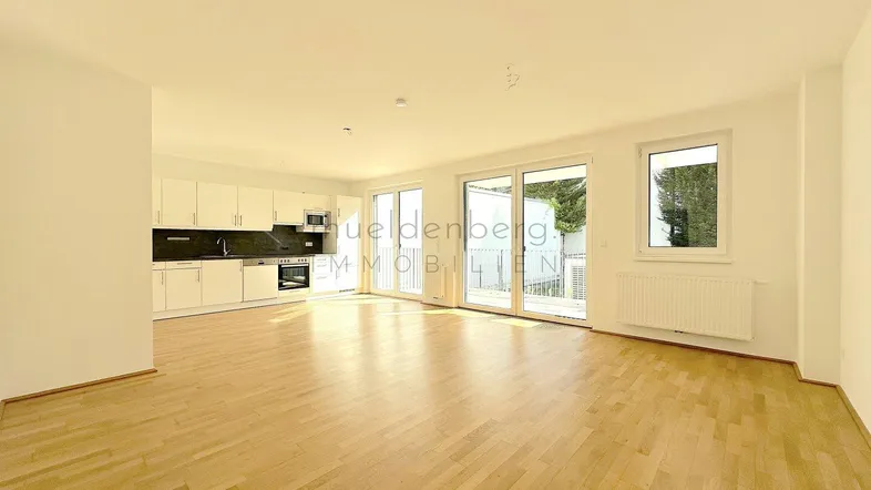 Heller offener Wohn- und Essbereich mit integrierter Küche, Parkettboden und Zugang zur Terrasse.