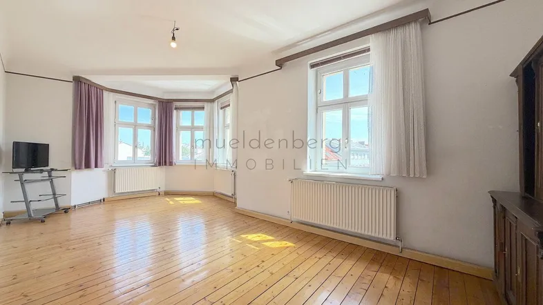 Helles Wohnzimmer mit Holzdielenboden, Erkerfenstern und viel Tageslicht.