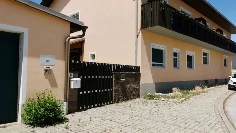 Ansicht des Gebäudes von außen mit gepflasterter Zufahrt und einem Nebengebäude.