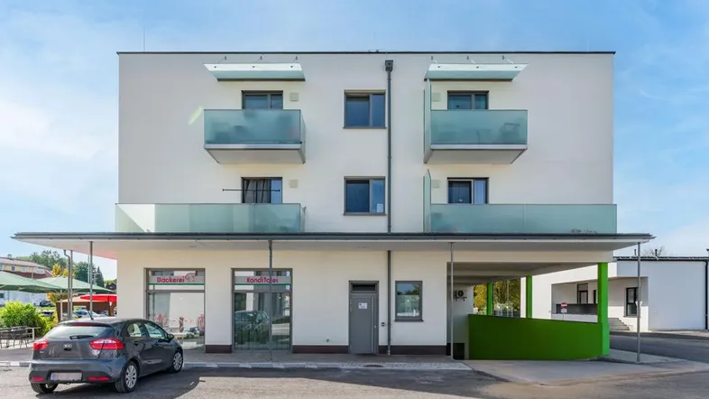 Modernes Mehrfamilienhaus mit Balkonen und Geschäften im Erdgeschoss unter blauem Himmel.