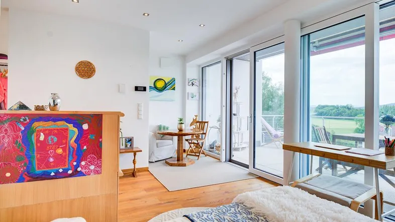 Helles Schlafzimmer mit Holzboden, großen Fenstern und Zugang zu einem Balkon mit Weitblick.
