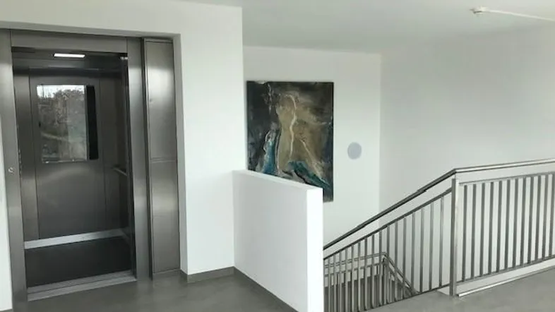Heller Flur mit modernem Aufzug und Treppenhaus, ausgestattet mit einem Kunstwerk.