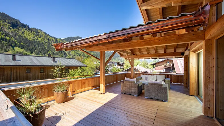 Große überdachte Holzterrasse mit bequemen Sitzmöbeln und herrlichem Blick auf die umliegenden Berge.