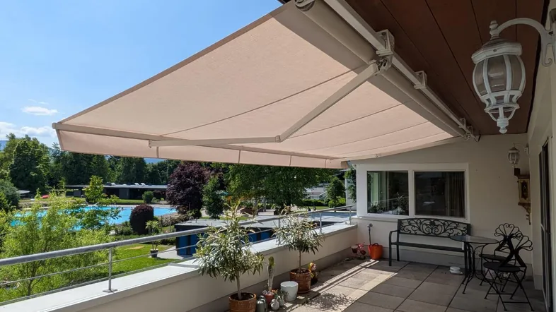Große Sonnenterrasse mit ausfahrbarer Markise, Gartenmöbeln und weitem Blick auf einen Poolbereich.