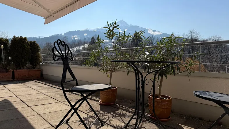 Sonniger Terrassenbereich mit Sitzgelegenheiten und beeindruckendem Bergblick im Hintergrund.