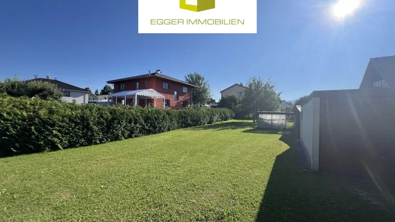 Großer, gepflegter Garten mit Rasenfläche, Hecke und einem Schuppen im sonnigen Außenbereich.