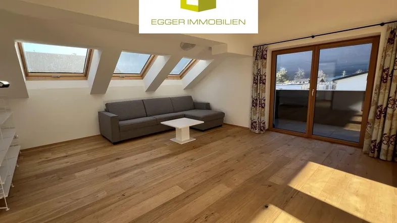 Helles Wohnzimmer im Dachgeschoss mit Holzboden, Dachfenstern und Zugang zum Balkon.