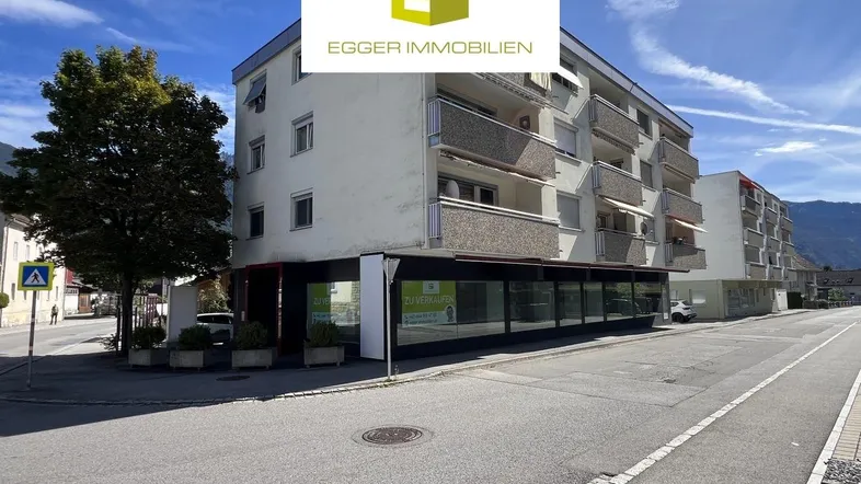 Mehrstöckiges Gebäude mit Geschäftsflächen im Erdgeschoss und Wohnungen darüber, an einer Straße gelegen.