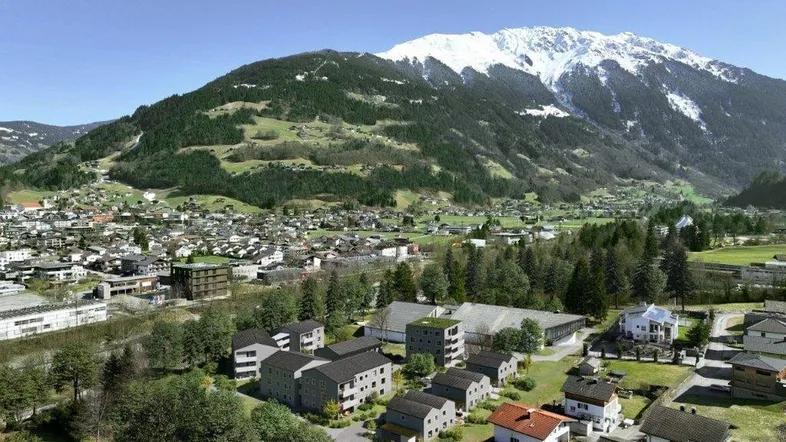 Panoramablick auf die Wohnsiedlung mit schneebedeckten Bergen und grünen Hügeln im Hintergrund.