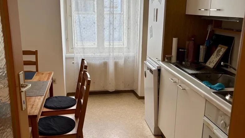 Funktionale Küche mit weißen Schränken, integrierten Geräten und einem Essbereich am Fenster.