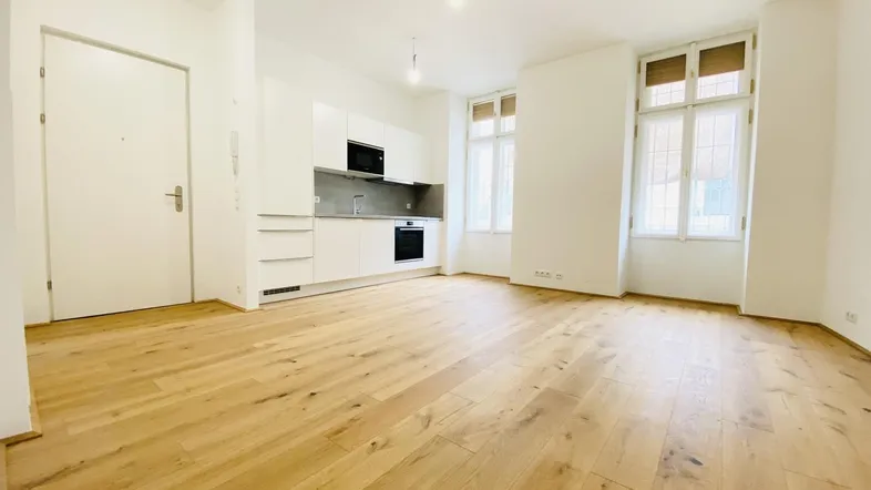 Heller Wohn- und Essbereich mit offener Küche, Parkettboden und großen Fenstern.