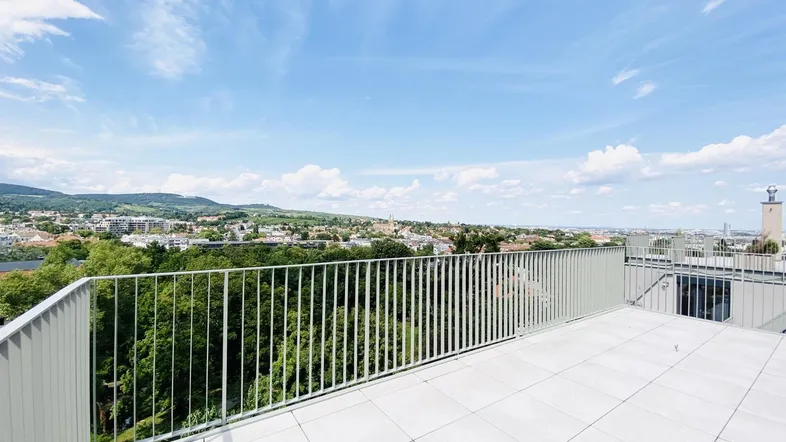 Große Dachterrasse mit hellen Fliesen, modernem Geländer und weitem Blick über die Stadt und Hügel.