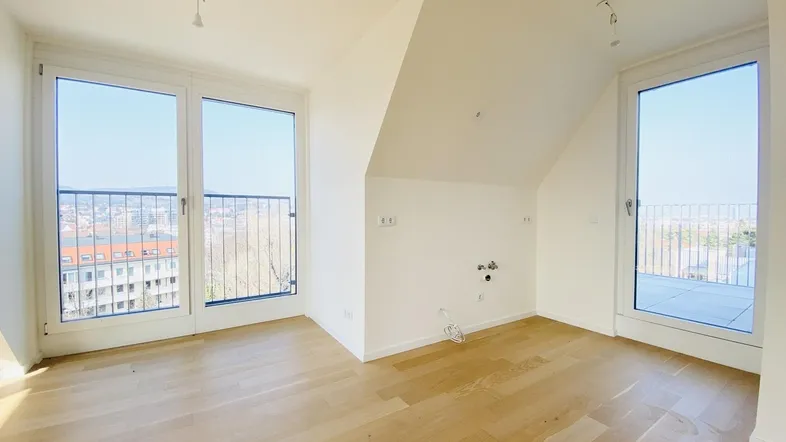 Heller Raum im Dachgeschoss mit Holzboden, großen Fenstern und Zugang zu einem Außenbereich.