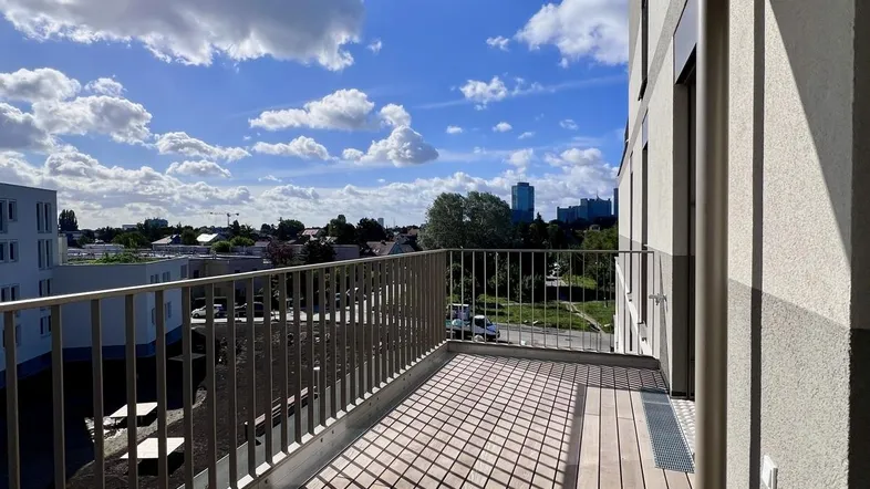 Heller Balkon mit Holzboden und Blick auf die Stadt und den blauen Himmel.