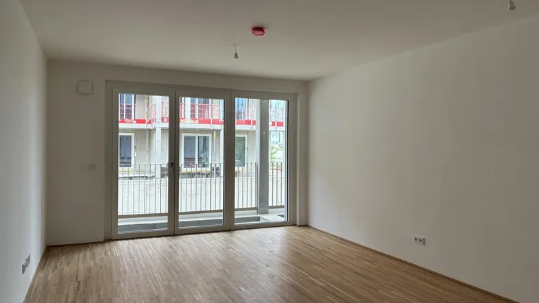 Heller, leerer Raum mit Holzboden und Zugang zu einem Balkon oder einer Loggia.