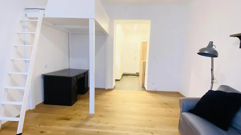 Helles Wohnzimmer mit Holzboden, Hochbett und integriertem Schreibtischbereich.