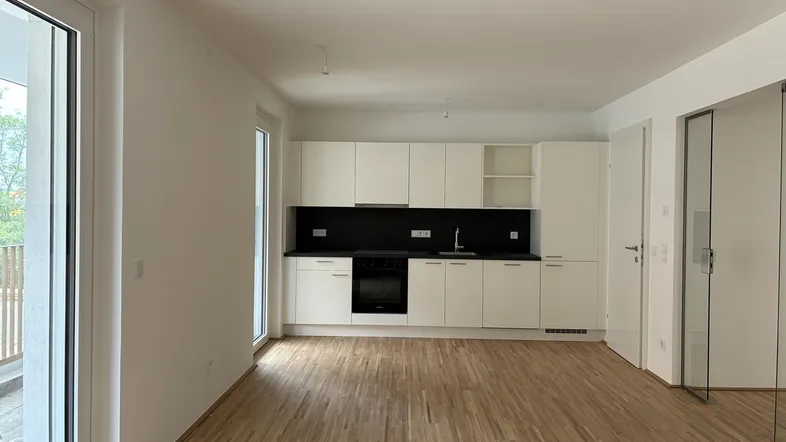 Heller offener Wohnbereich mit integrierter Küche, weißen Schränken und Holzboden.