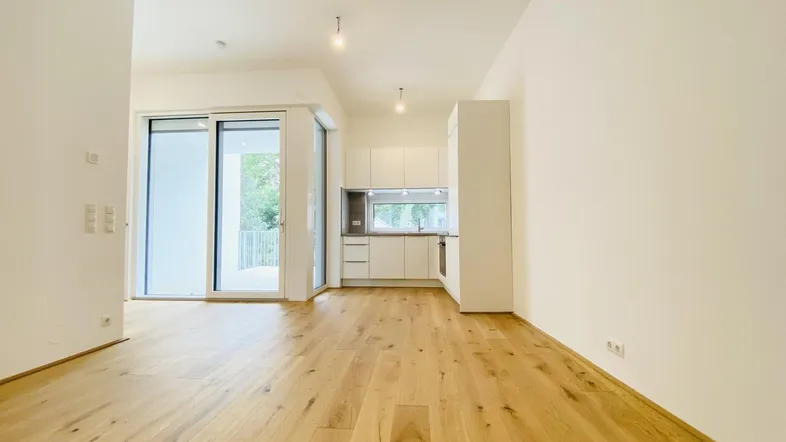 Heller offener Wohnbereich mit moderner Einbauküche, Holzboden und Zugang zum Balkon.