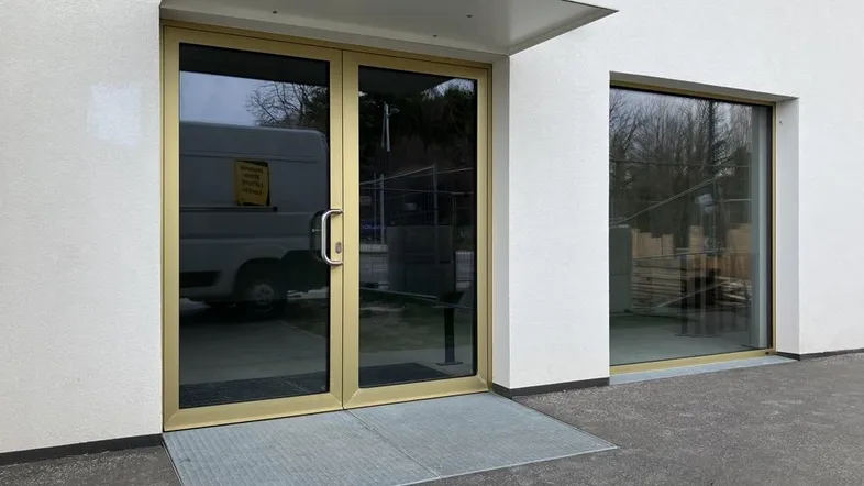 Moderner Eingangsbereich mit goldfarbenen Türen und einer barrierefreien Rampe.