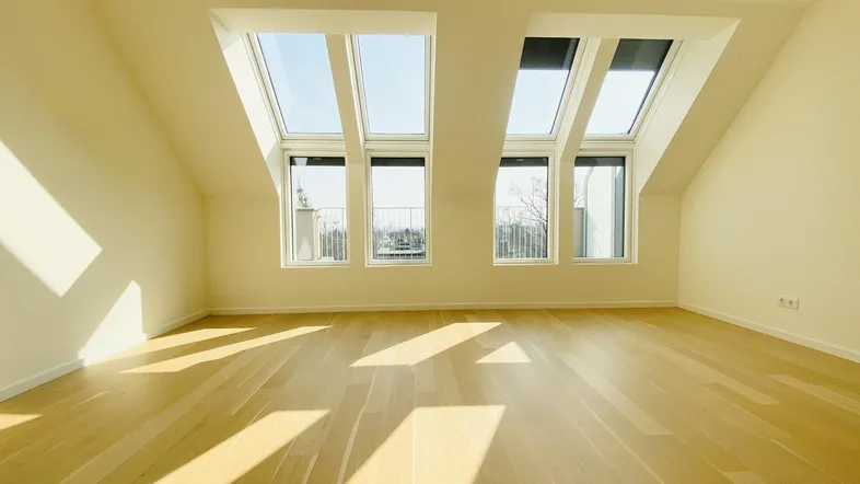Helles Dachgeschosszimmer mit großen Dachfenstern und Holzboden, durchflutet von Sonnenlicht.
