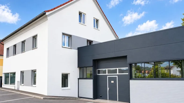 Modernes Geschäftsgebäude mit weißer Fassade und dunkelgrauem Anbau unter blauem Himmel.