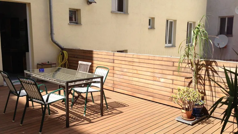 Sonnige Terrasse mit Holzboden, Esstisch und Pflanzen, ideal für entspannte Stunden im Freien.