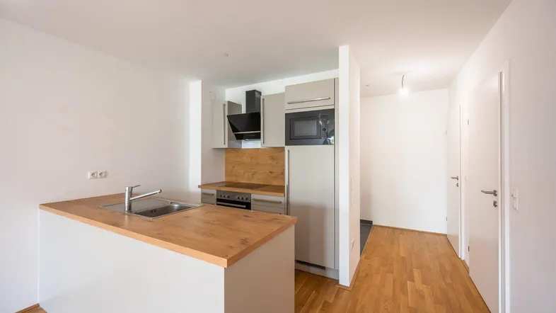 Moderne Küchenzeile mit Holzarbeitsplatte, Spüle, Kochfeld und integrierten Geräten in hellem Design.