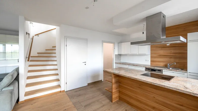 Moderne Küche mit Kochinsel, Granitarbeitsplatte und Holztreppe zum oberen Stockwerk.